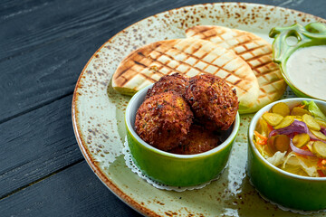 A Appetizing oriental dish, falafel with pita bread, served with white sauce and pickles in a green plate against a dark, woody background. Vegetarian food