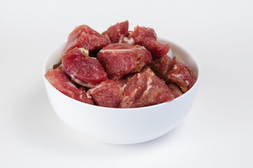 Ceramic bowl with raw marinated meat on a white background. Pieces of pork with salt, pepper and granulated garlic.