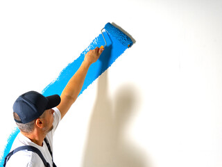 Male painter painting a white wall with a roller in blue color renovations or construction concept.