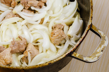 Meat with onions in the cauldron close-up. Chunks of pork mixed with onions are fried in a...