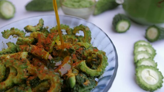Oil pouring on Karela slices mixed with Haldi to make Achaar - Indian recipe. Closeup shot of sliced bittermelon  Karela paste  and the vegetable juice together against a white background