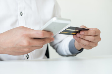 The businessman's hand is holding a credit card and using a smartphone for online shopping and internet payment in the office