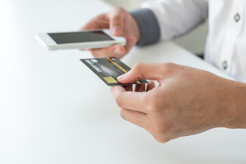 The businessman's hand is holding a credit card and using a smartphone for online shopping and internet payment in the office