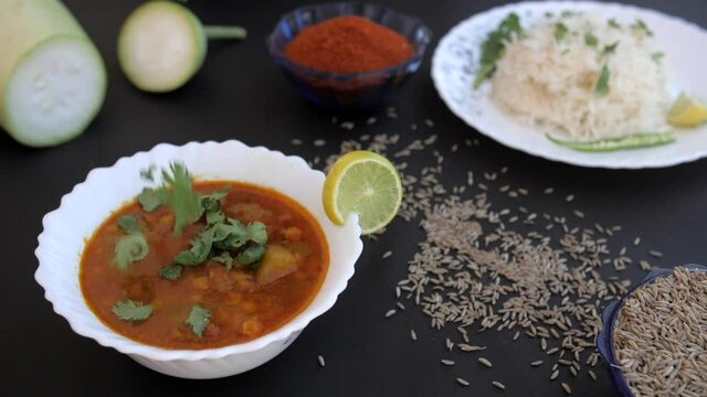Tasty bottle gourd curry garnished with fresh coriander leaves served for lunch. Closeup shot of sliced Lauki  chili powder  and Jeera scattered on the table against a black background