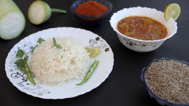 Fresh Coriander Leaf / Dhania Falling On A Plate Of White Rice With Green Chilies. Closeup Shot Of A Bowl Of Tasty Ghiya Curry Decorated With A Slice Of Lemon  And Cumin Seeds Against A Black Backg...