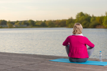 Back View of Mature Caucasian Blond Woman During Yoga Practice on Blue Mat At Water Shore Outdoor.