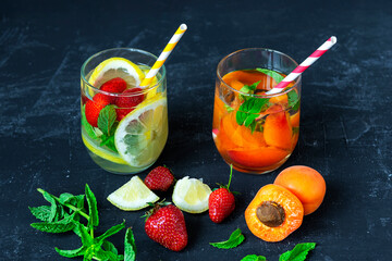 Refreshing summer drinks with lemon, strawberry and apricot slices in glasses on black background