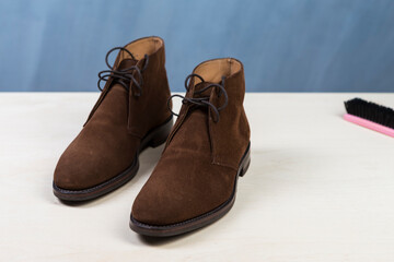 Pair of Mens Suede Brown High Boots Along With Cleaning Brush on Table Surface.
