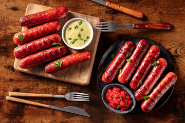 Sausages with ketchup and mustard sauce, overhead flat lay shot on a dark rustic wooden table. Bbq...