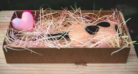 Toy plush guitar and a pink heart in a gift box filled with colorful paper strips, anniversary day celebration beautiful gift idea.