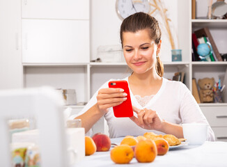 Portrait of young woman housewife using phone at home kitchen