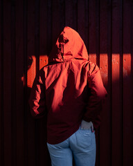 Young woman standing back in red clothes in front of red wall. Monochrome, Hard sunlight and shadows