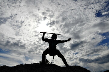 Warrior in armor with a sword over his head against the background of the sky
