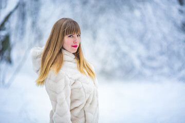 Beautiful smiling confident young white woman pretty face in a white fur coat looking at camera posing alone at snowy forest