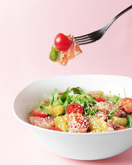 Fresh salad with shrimp and vegetables close up in a bowl over pastel pink background.