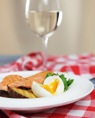 Salmon steak with fresh greenery and boiled eggs served on a white plate with a glass of wine.