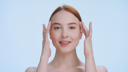 Young attractive ginger woman touches her face runs fingers from under her eyes up to her temples...