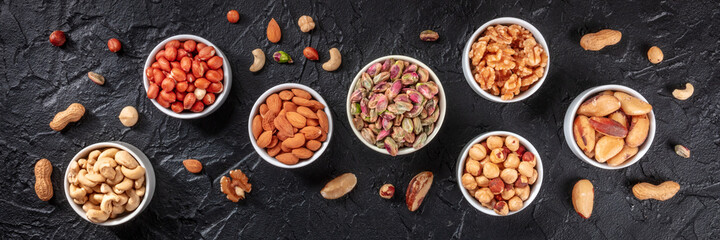 Nuts panorama, top shot on a dark background. Healthy vegan snacks