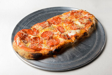 Pizza with bacon, salami and cheese served on a metal tray over white background.