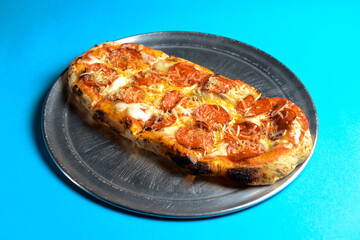 Pizza with bacon, salami and cheese served on a metal tray over blue background.