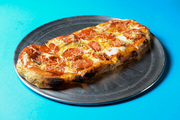 Pizza with bacon, salami and cheese served on a metal tray over blue background.