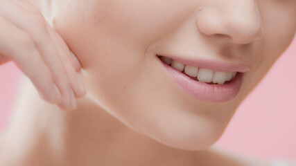 Extreme close-up of female skincare model touches her jawline smiling wide for the camera against pink background | Moisturizer wearing shot for skincare commercial