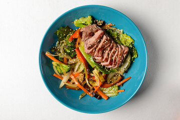 Fresh summer salad with stripes of fried beef and avocado slices, radish, sprouts, broccoli and ginger