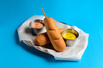 Corndogs with two different kinds of sauce served on a metal tray over blue background.