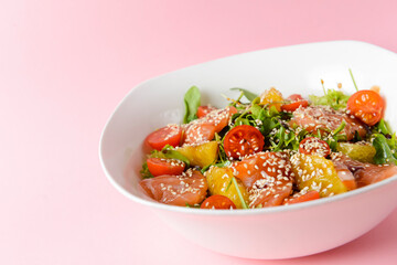 Fresh salad with salmon and vegetables close up in a bowl over pastel pink background.