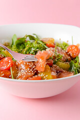Fresh salad with salmon and vegetables close up in a bowl over pastel pink background.