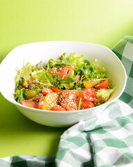 Fresh salad with salmon and vegetables close up in a bowl over bright green background with tablecloth.