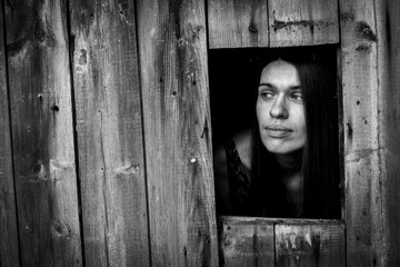 A young woman in a window ща wooden building. Black and white photo.