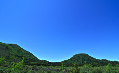 Fototapeta na wymiar 雲の無い快晴の青空と緑の山。