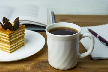 Cup of coffee , biscuit cake, book and notebook on wooden table. Coffee break and relaxation.