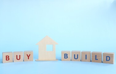 Buy or build a house concept. Wooden house model with wooden blocks in blue background.