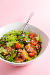 Fresh salad with salmon and vegetables close up in a bowl over pastel pink background.