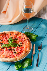 Fresh italian pizza with salami and black olives and other food on the background. Blue colored wooden table.