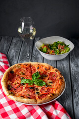 Fresh italian pizza with salami and black olives served with a glass of white wine.