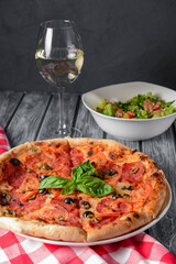 Fresh italian pizza with salami and black olives served with a glass of white wine.