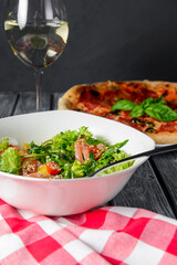 Fresh italian pizza with salami and black olives served with a glass of white wine.