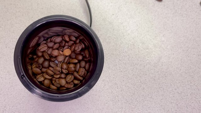 Freshly roasted coffee beans are poured into a coffee grinder. Barista prepares coffee for grinding close-up. Top view with space for text. Slow motion.