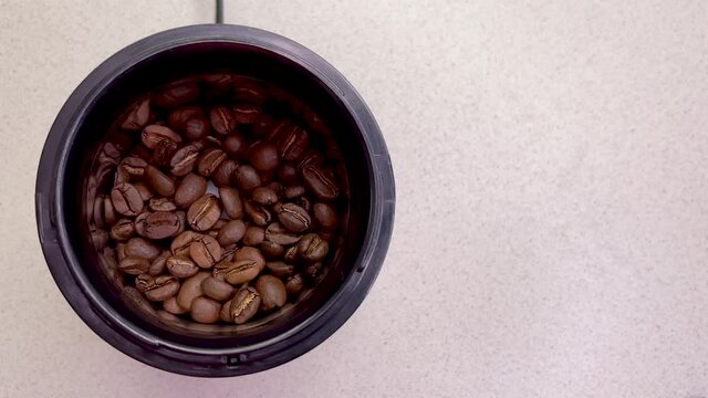 Freshly roasted coffee beans are poured into a coffee grinder. Barista prepares coffee for grinding close-up. Top view with space for text. Slow motion.