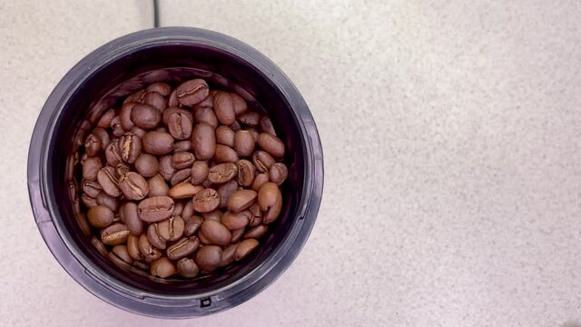 Freshly roasted coffee beans are poured into a coffee grinder. Barista prepares coffee for grinding close-up. Top view with space for text. Slow motion.