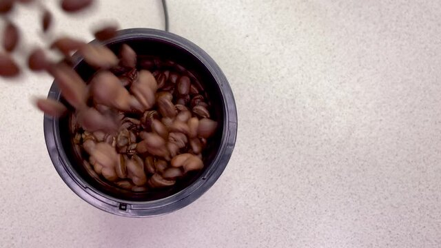 Freshly roasted coffee beans are poured into a coffee grinder. Barista prepares coffee for grinding close-up. Top view with space for text. Slow motion.