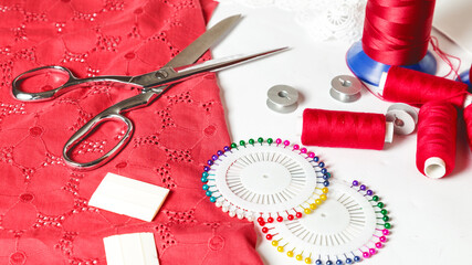 different sewing accessories on the table. Threads, pins, chalk, spools, red cloth and sewing scissors close-up on a white table background