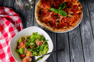 Fresh italian pizza with salami and black olives and fresh vegetable salad. Traditional Italian pizza recipe