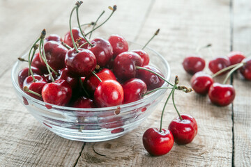 Ripe sweet cherries in a glass bowl on wooden table with green bokeh background, summer fruits
