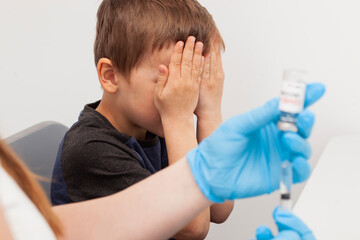 The child fears the injection. Boy covered his face with his hands because scared of vaccination