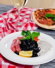 Squid Ink Black Pasta with seafood served on a white plate with a glass of white wine.