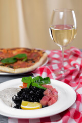 Squid Ink Black Pasta with seafood served on a white plate with a glass of white wine.